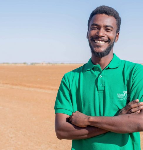 رجل يلبس قميصا أخضر به شعار شركة ماتوقرين الزراعية في صحراء نهارا والسماء صافية